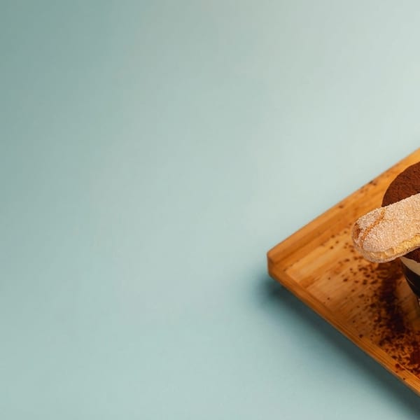 Tiramisu dessert in a glass with a ladyfinger cookie on top, served on a wooden tray.