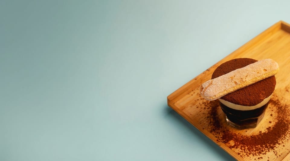 Tiramisu dessert in a glass with a ladyfinger cookie on top, served on a wooden tray.