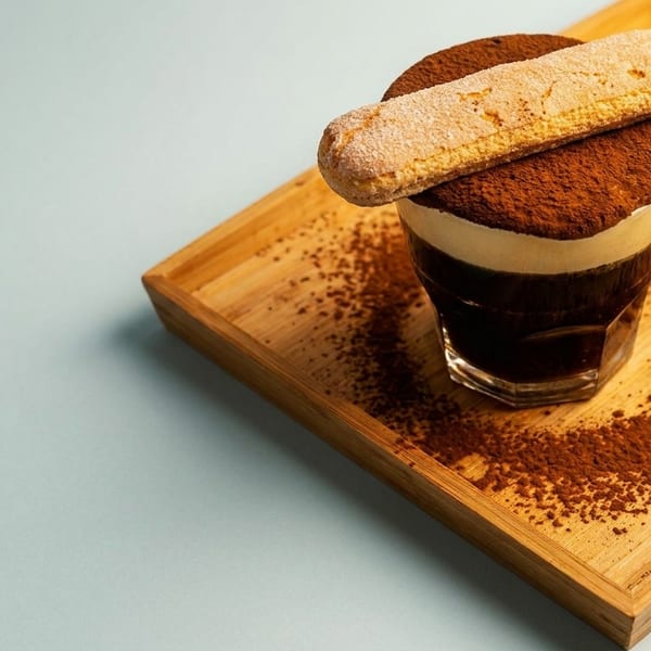 Tiramisu dessert in a glass, topped with cocoa powder and a ladyfinger, on a wooden tray.