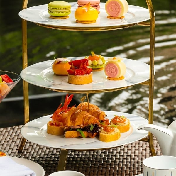 Afternoon tea with a three-tiered stand of pastries, savories, and fruit cocktails by a pond.