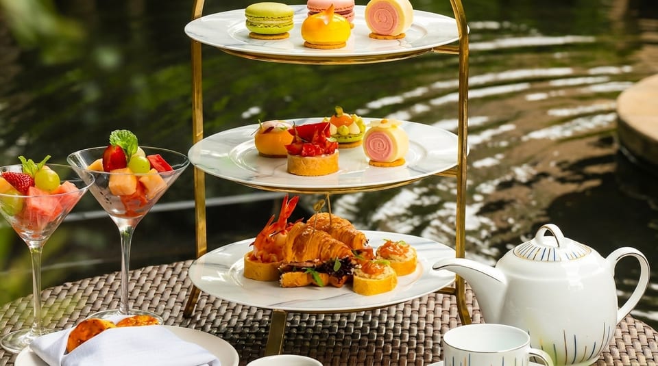 Afternoon tea with a three-tiered stand of pastries, savories, and fruit cocktails by a pond.