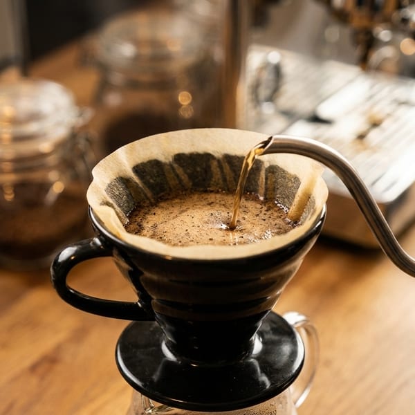 Pour-over coffee being brewed, with hot water from a gooseneck kettle filling a filter.